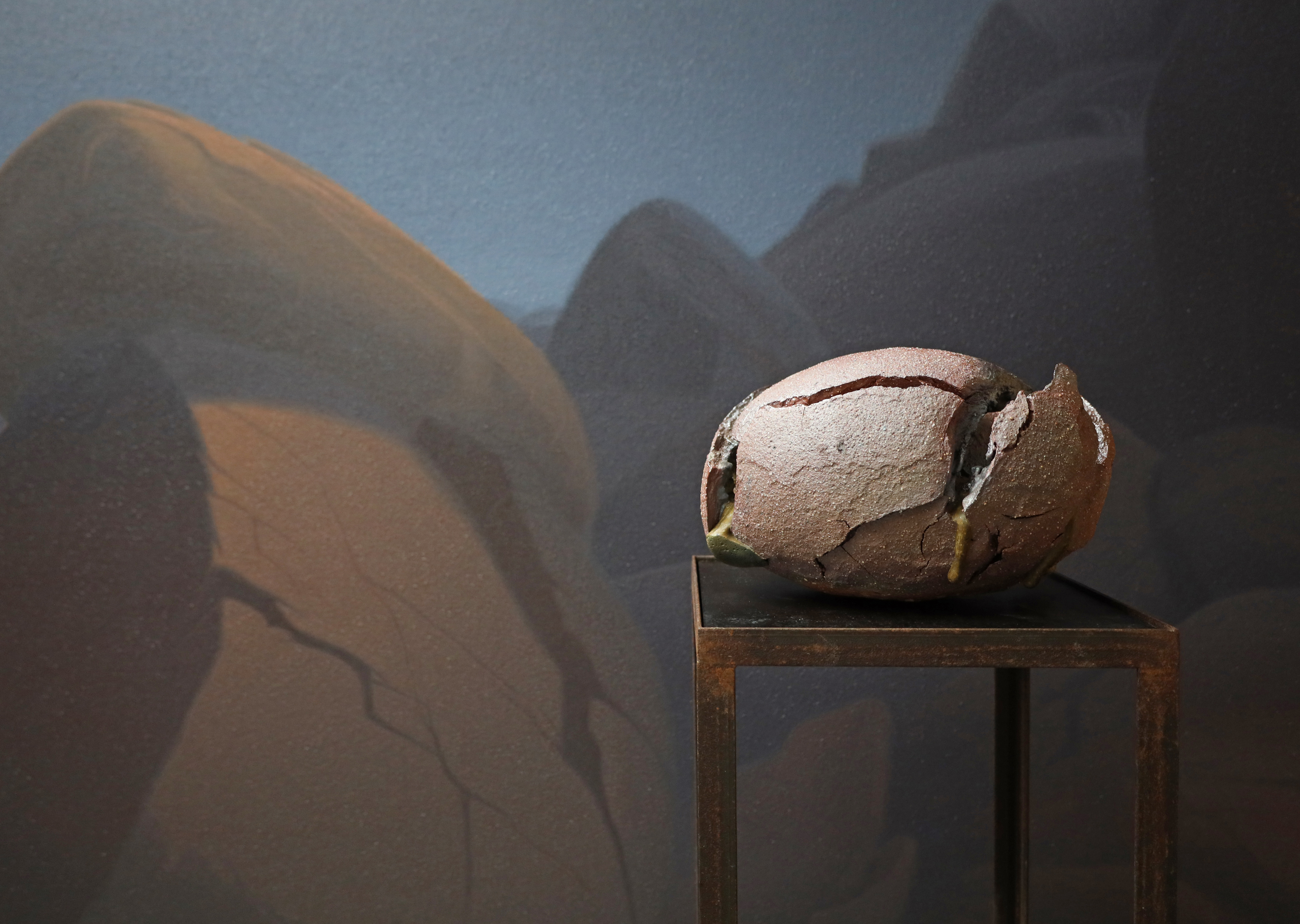 ovales Keramik-Objekt vor gemalter Wüstenlandschaft in Braun und Blau