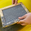 Zwei Hände schöpfen Papierbrei in Rahmen in gelber Wanne Zwei Hände schöpfen Papierbrei in Rahmen in gelber Wanne