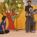 Theaterszene mit Baum, Frau, Mann und Stofftierelefant Theaterszene mit Baum, Frau, Mann und Stofftierelefant