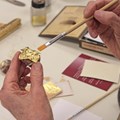 Hände halten Pinsel und kleines Objekt mit Goldplättchen Hände halten Pinsel und kleines Objekt mit Goldplättchen