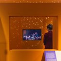 Besucherin neben Monitor mit Videos versch. Ensembles