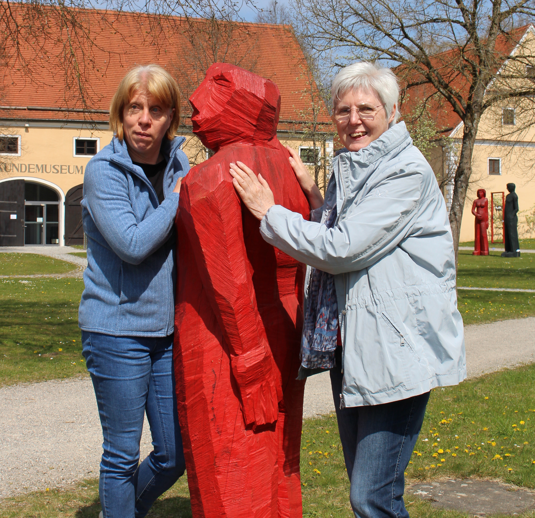 zwei Frauen fühlen an der Oberfläche einer roten Holzskulptur