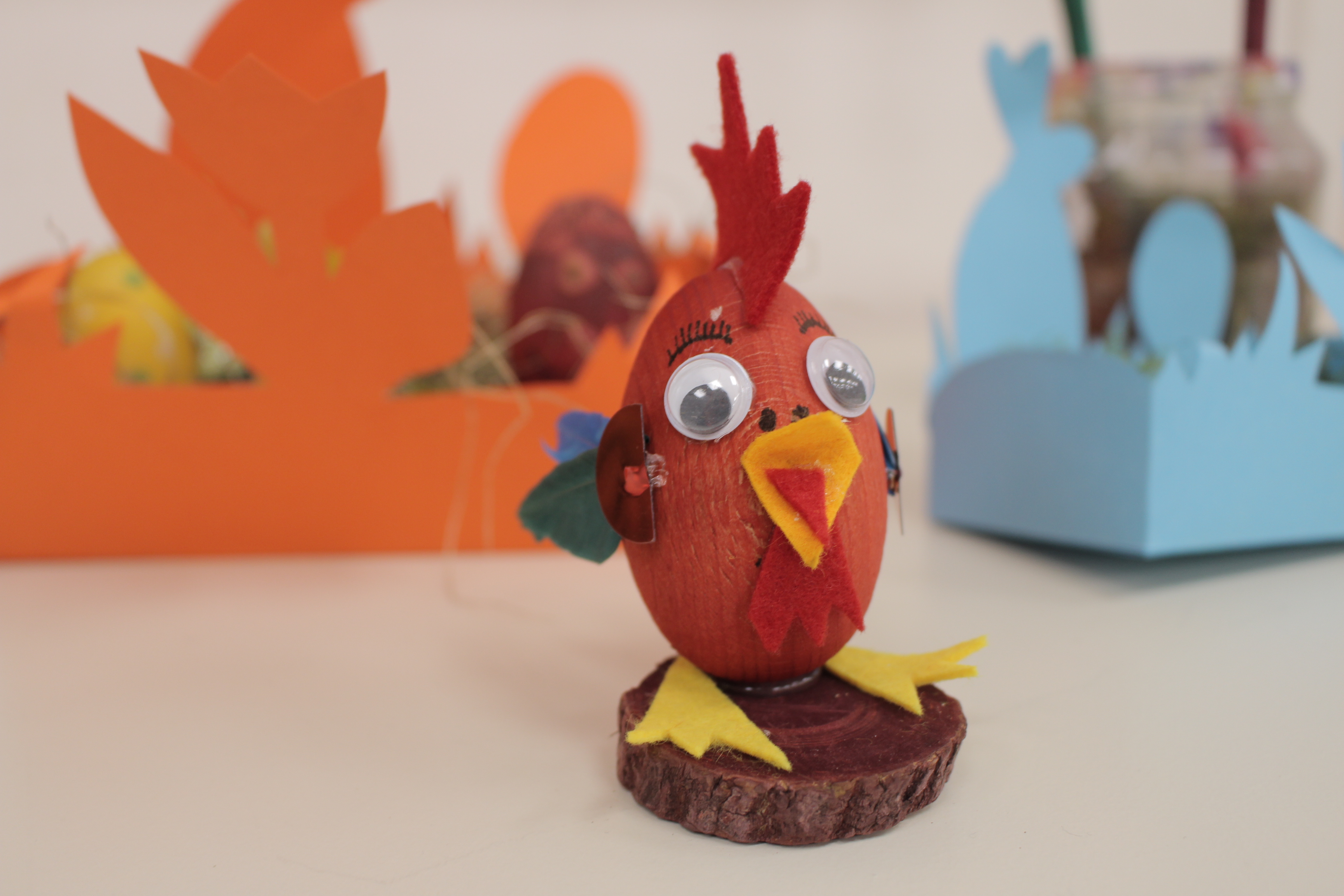Rotes Ei mit Schnabel, Augen und Füßen beklebt und als Küken gestaltet