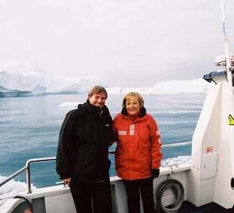 Daniel Biskup und Angela Merkel mit roter Jacke auf einem Schiff, dahinter Meer und Eisberge